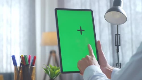 Close up of man's hand using a mock up green screen tablet on a desk at office