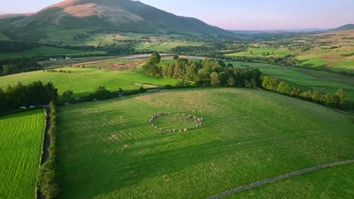 Ancien cercle de pierre dans un champ vert avec de longues ombres à l'heure dorée et vue sur la montagne lointaine Bl