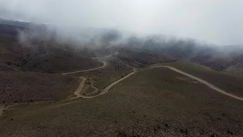 Car drives dirt road winding through foggy rolling hills in Argentina
