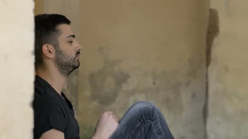 Man Sitting Against Wall in Empty Room