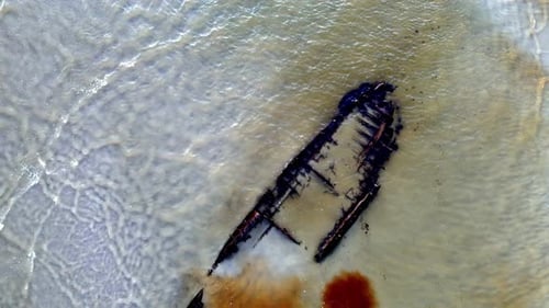 Luftaufnahme eines Schiffswracks an einem Strand mit türkisfarbenem Wasser, rostfarbenem Metall auf dem Schiff und Weiß