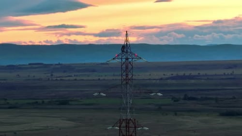 Aerial view showing electricity pylon on rural field in front of hills at sunset