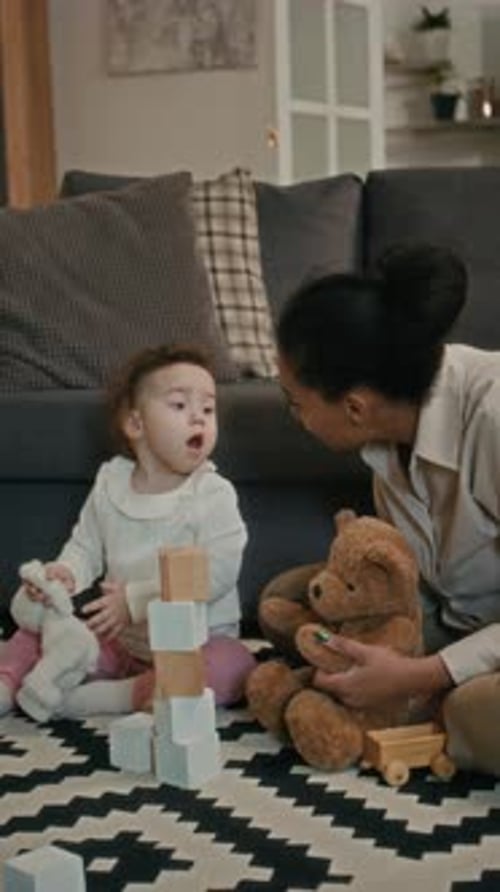 Baby Playing with Blocks Next to Adult with Toys