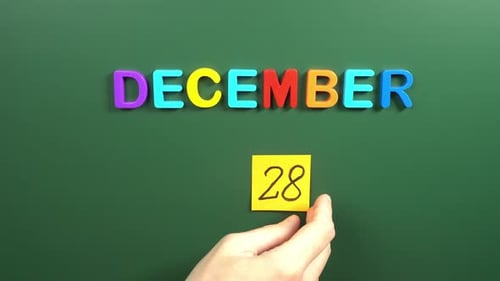 Hand sticking a sticker 28 December calendar day on school board. 28 date of December. Twenty