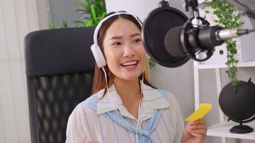 Jovem DJ de áudio asiática falando ao microfone para transmitir.