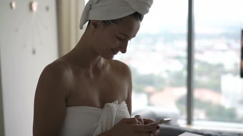 Woman in towel using phone after shower
