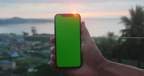 Close Up Holding Smartphone in Vertical Position with Green Screen Chroma Key Over Sunset at Sea at