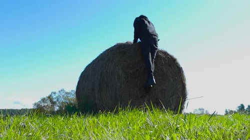Man runs towards and jumps on a round hay bale in slow motion making hay move and fall during summer