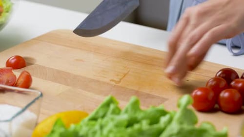 Woman cuts cherry tomatoes on wooden cutting board