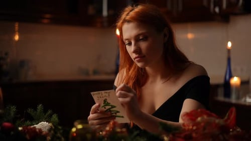 A Beautiful Redhaired Woman Sitting at a Festive Table Draws Something with a Ballpoint Pen on a New
