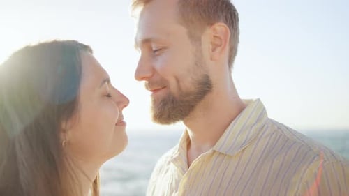 A Couple Stands Together By the Ocean Embracing Each Other Warmly As the Sun Sets in the Background