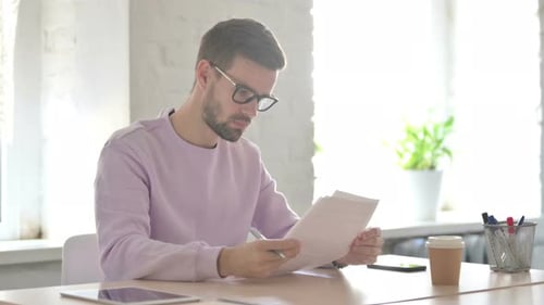 Young Man Reading Reports While Sitting in Office