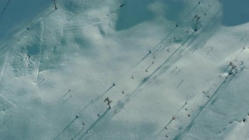 Aerial: tourists skiing and snowboarding down ski run under chairlifts, top down
