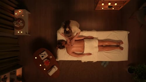 Blick von oben auf den Spa-Salon: Frau liegt auf dem Massagetisch, Therapeutin macht ihren vollen Rücken