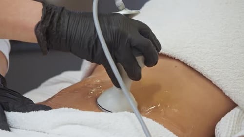 Cosmetologist is Performing Skin Treatment on Person's Stomach Area Person is Resting on Couch with