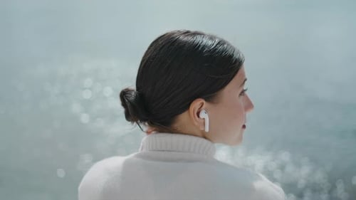 Woman Tourist Listening Music in Wireless Earbuds Sitting at Lake Water Close Up