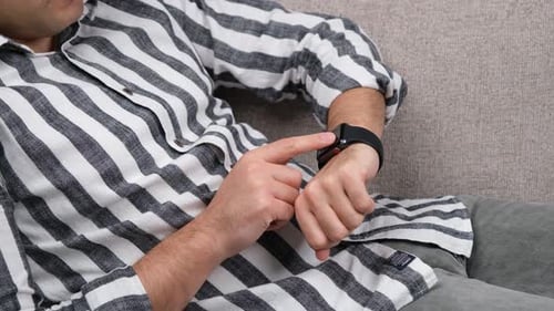 Man Taps Smartwatch Screen While Relaxing on Couch