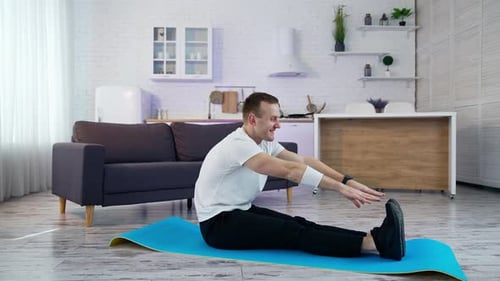 Man Stretches Hamstrings on Yoga Mat at Home