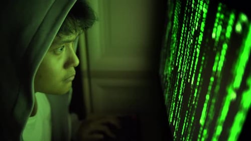 Un hacker cagoulé utilise un ordinateur avec un Code vert la nuit