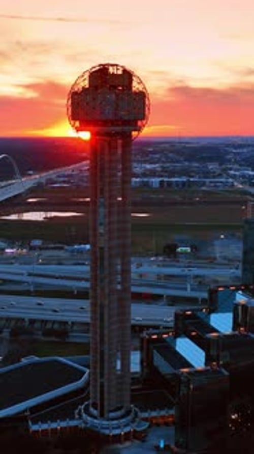 Reunion Tower switching on lights at sunset. Multiple cars drive by the roads