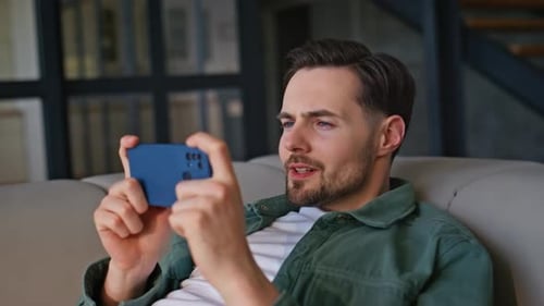 Man Laughing at Phone on Couch at Home