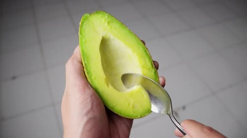 Closeup of fresh green avocado flesh being scooped out using spoon