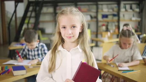 Portrait of an Elementary School Girl Standing in the Foreground Holding Textbooks Looking at the