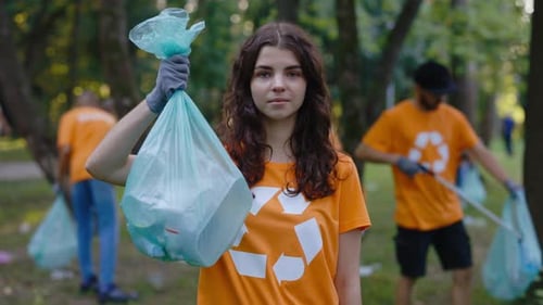 Retrato de mujer joven caucásica con camiseta con símbolo de reciclaje, bolsa llena de basura