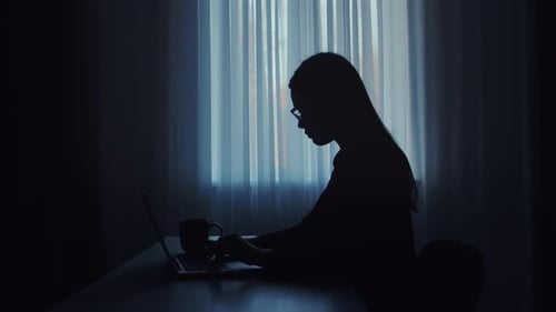 Silhouette of Woman Working Late on Laptop with Coffee