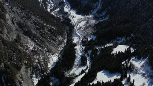 Beautiful mountain road between trees, surrounded by huge mountains, aerial shot in 4k