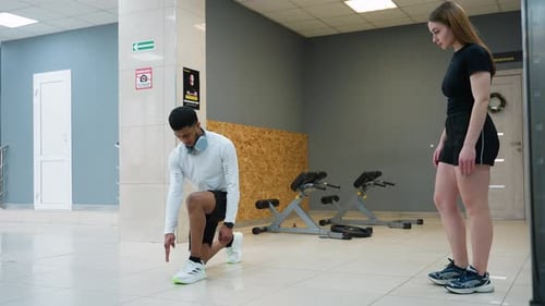 Female Trainee Observes Instructor Demonstrating Lunge Form During Gym Training Session
