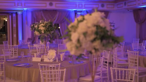 Close-up shot of elegant white flower bouquets arranged on restaurant tables, illuminated by warm li