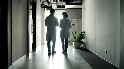 Doctors walking down hospital corridor discussing medical procedures and patient care.