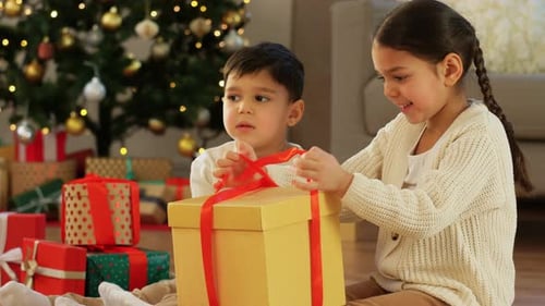 Children opening gift by illuminated Christmas tree