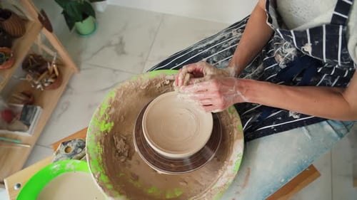 Femme potière en jean et tablier travaillant sur un tour de potier fabriquant une carafe en céramique