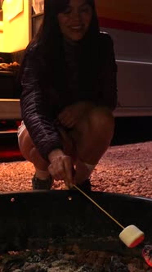 Young Woman Roasting a Marshmallow Over a Campfire at Night