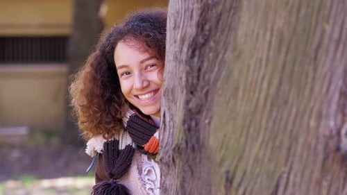 Woman Smiling, Peeking Behind a Tree in Park