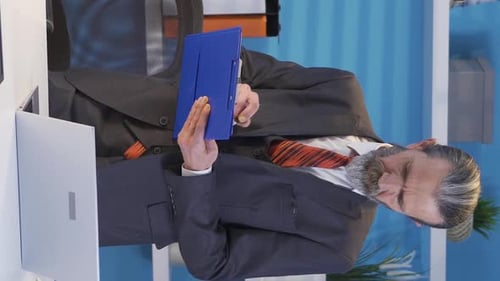 Vertical Video of Mature businessman working on laptop in office taking notes.