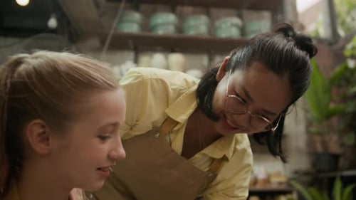Cheerful Teacher Instructing Young Girl Crafting Clay Pot in Workshop