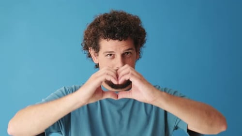 Close up, man showing representing heart gesture isolated on blue background in studio