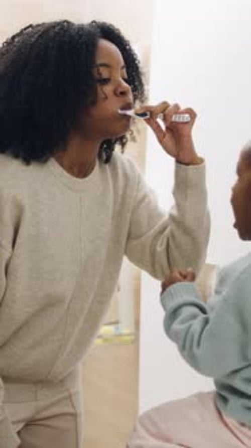 Mother Brushing Teeth with Child Watching in Bathroom