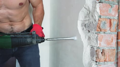 Worker Using Demolition Hammer to Break Brick Wall During Apartment Renovation