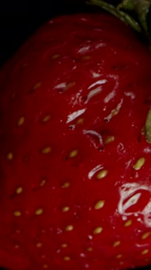 Vertical video. Slow-Motion Fall of a Strawberry, a Hand Catches It with Two Fingers, Top View .