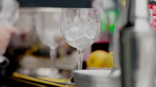 Bartender preparing drinks, ice-filled glasses lined up on a bar counter, close up shot.