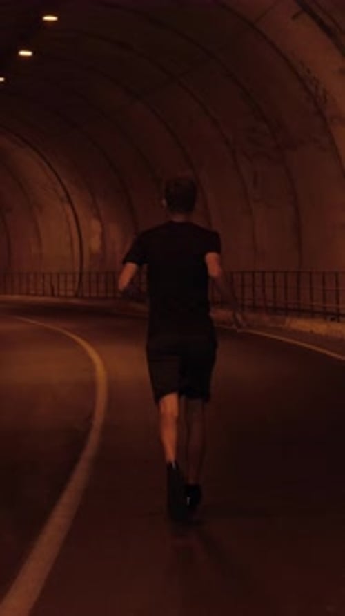 Male athlete running through empty tunnel in high mountain range. Vertical video