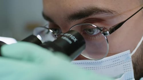 Eyes of Male Scientist Looking through Microscope in Lab