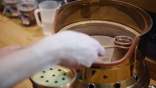 Nahaufnahme von Händen, die eine metallische Tasse mit Kaffee halten und auf den Zutaten Kreise ziehen