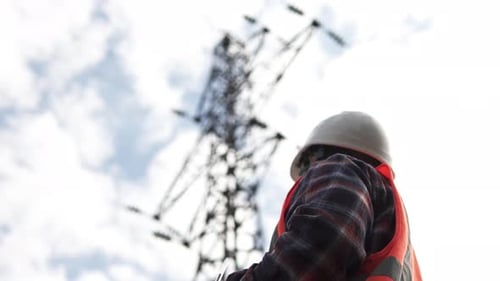 Engineer Writing On Clipboard Near Transmission Tower
