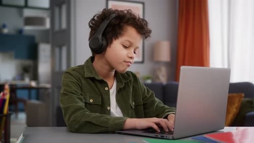 Child Wears Headphones Typing on Laptop at Desk