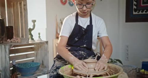 Young Teen Boy Sitting Potter's Wheel Looking Into the Camera Smiling Engaged in Pottery Creates a